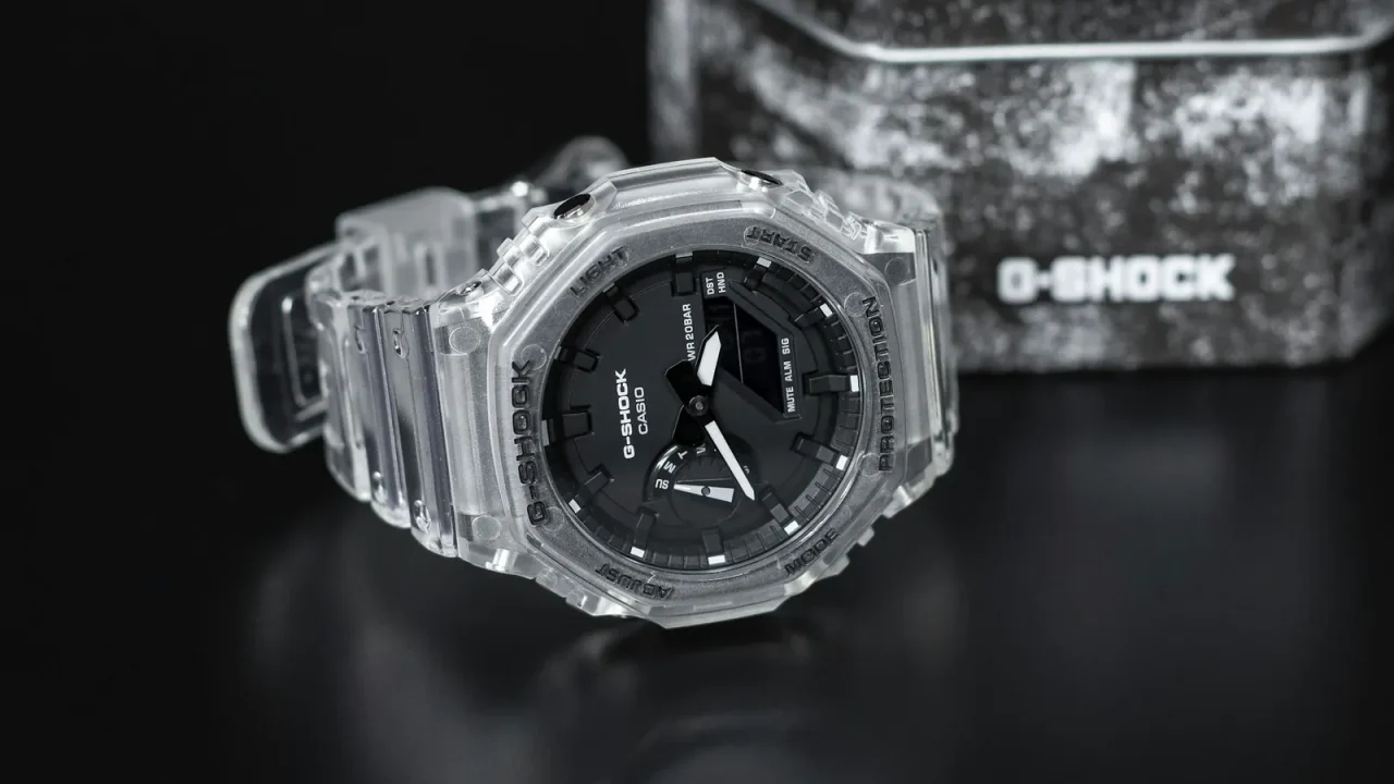 Analog-digital watch with a clear resin case displayed beside its storage tin