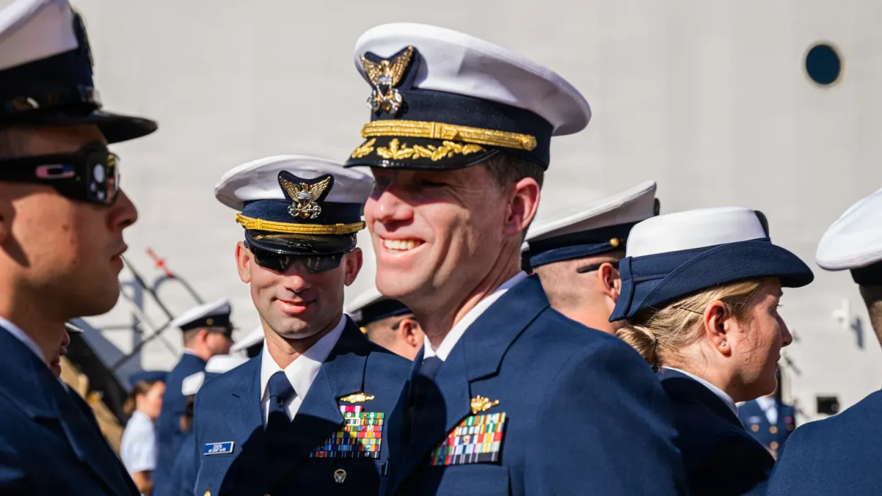 Coast Guard officers in dress uniforms and white combination caps smile during a change of command ceremony