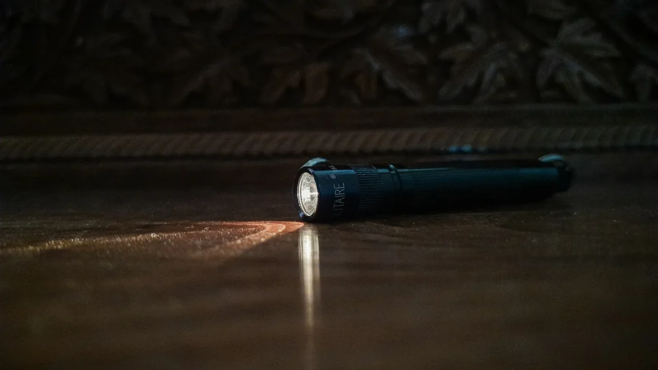 Compact black flashlight lying on a dark floor with its beam switched on