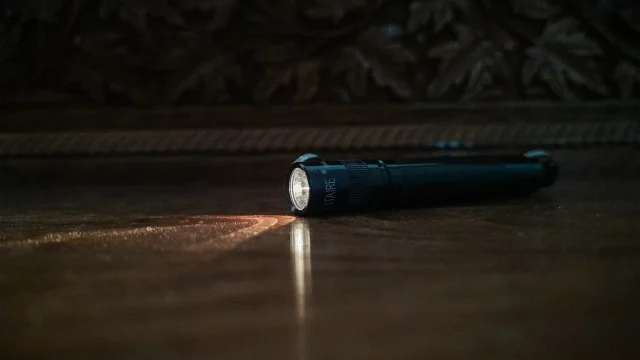 Compact black flashlight lying on a dark floor with its beam switched on