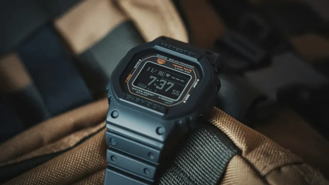 Black digital watch with a resin strap resting on a canvas backpack