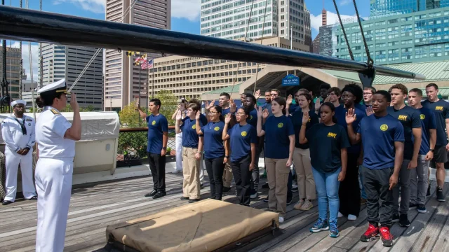 Group of future sailors in Navy T-shirts raise their right hands to take the oath of enlistment