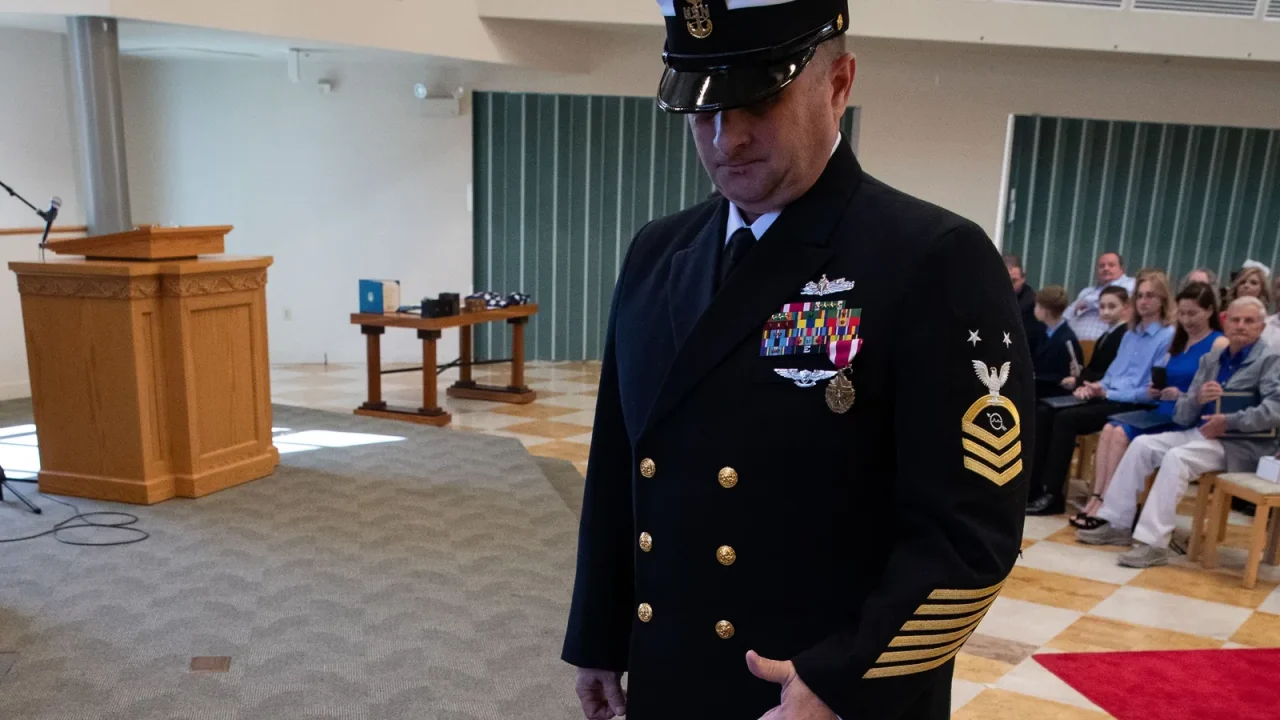 Navy master chief in dress blues looks down at a shadow box during his retirement ceremony