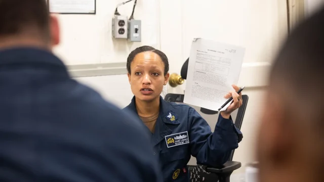 A Navy career counselor holds up paperwork while speaking to sailors during a Career Development Board aboard a ship