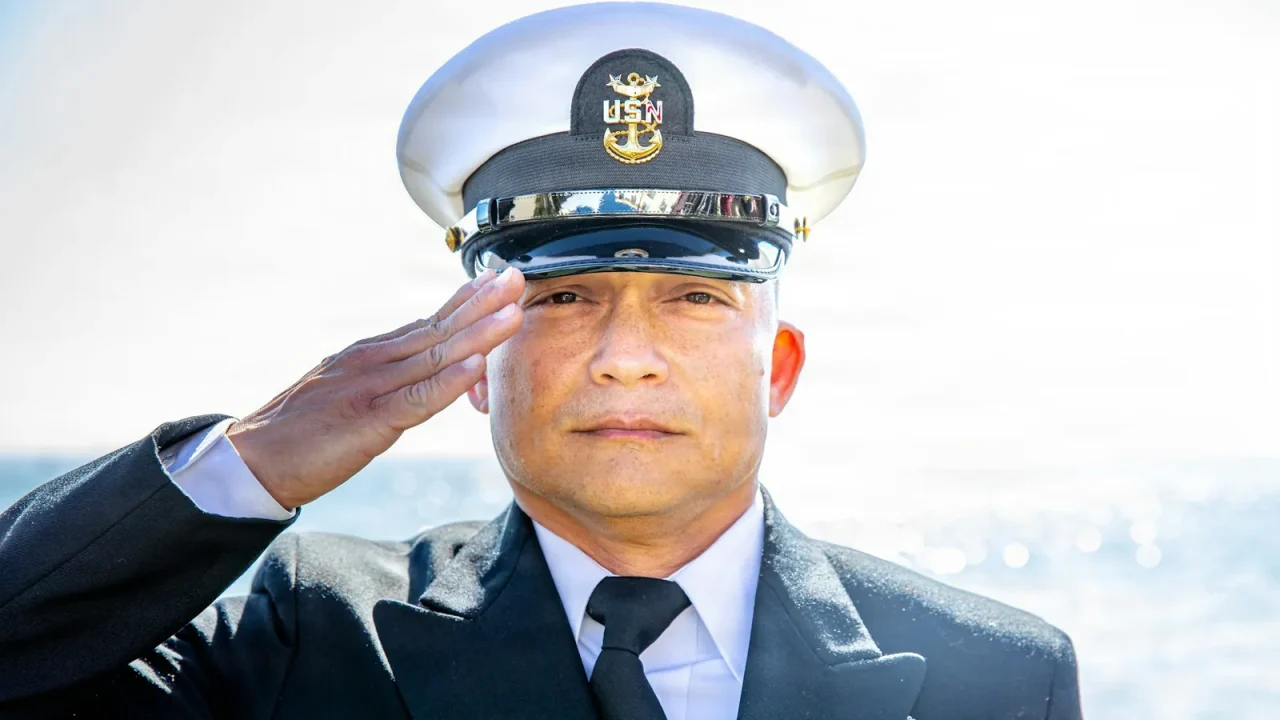 Navy chief petty officer in a dress blue uniform and combination cap salutes outdoors