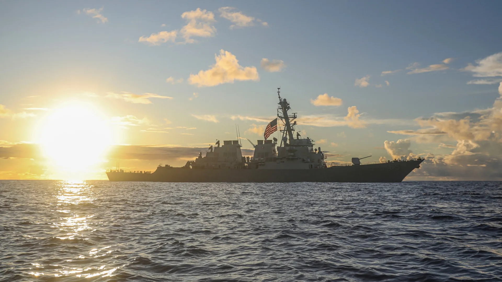Navy destroyer underway at sunset with the American flag flying from its mast