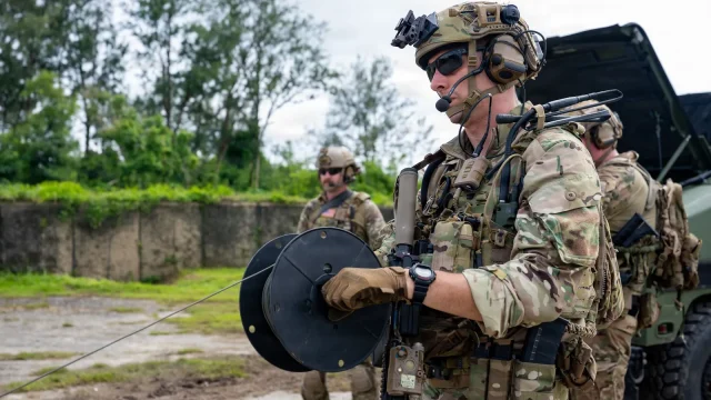 A Navy explosive ordnance disposal technician in combat gear holds a spool of tubing during a training drill on Guam