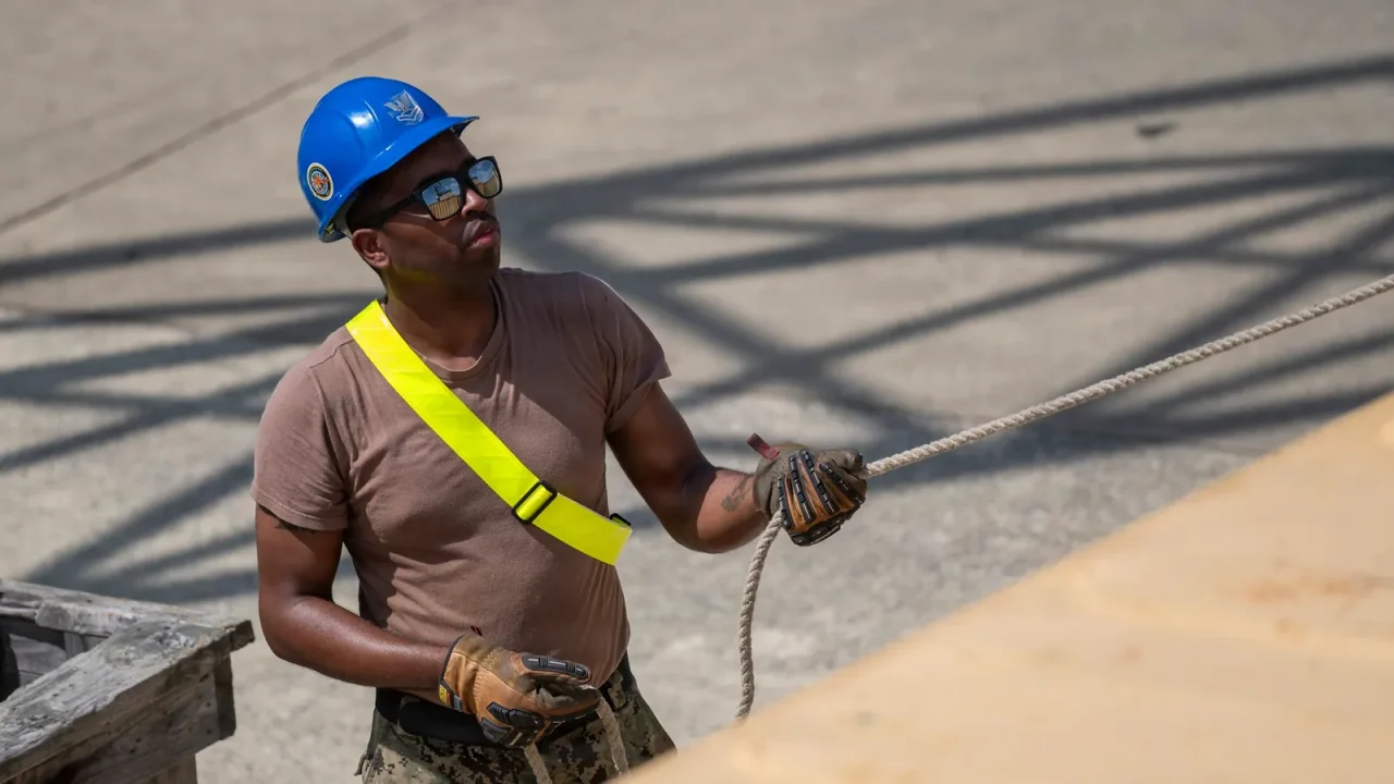 A Navy sailor in a hard hat guides a cargo lift with a rope during mobilization training in Virginia