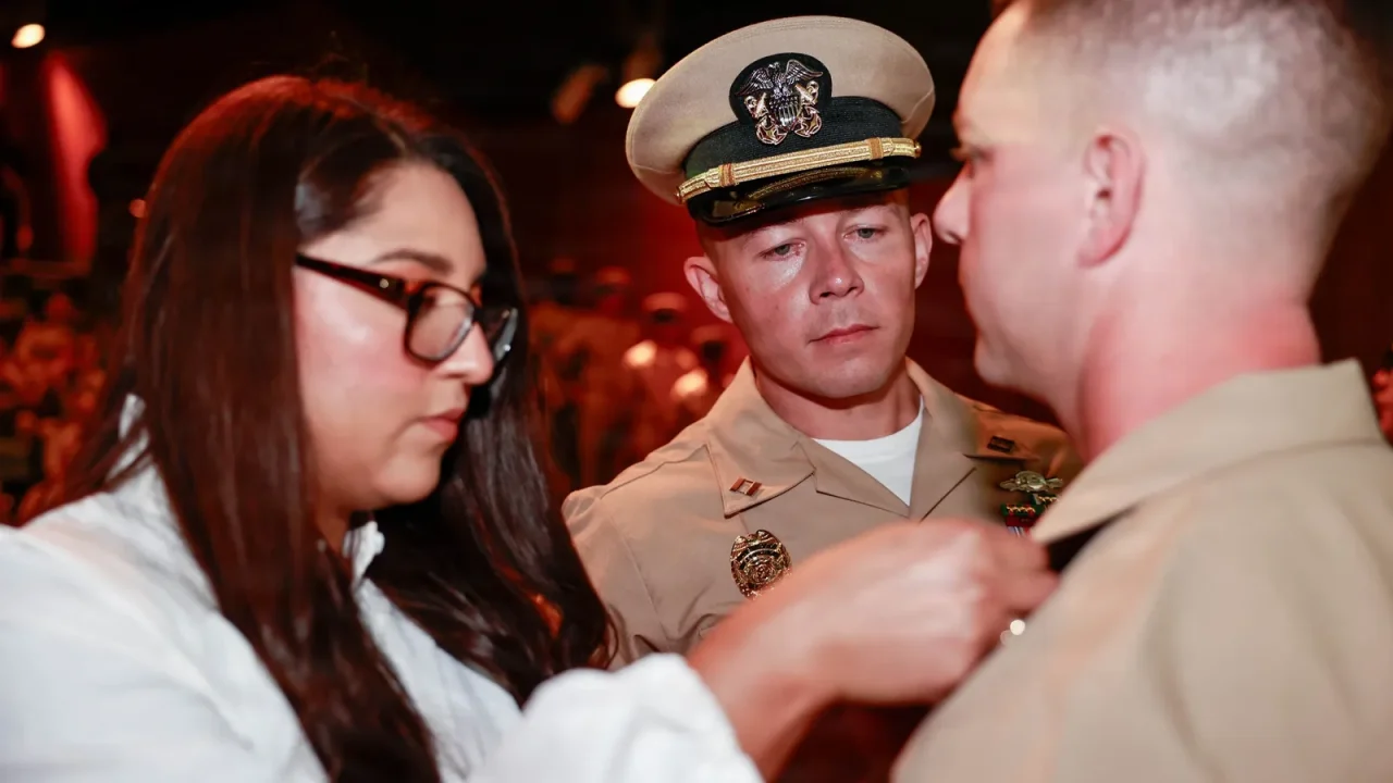 A new Navy chief petty officer in khaki uniform is pinned with his anchors by a family member at a pinning ceremony