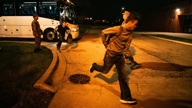 New recruits in civilian clothes hurry off a bus at night as they arrive at boot camp