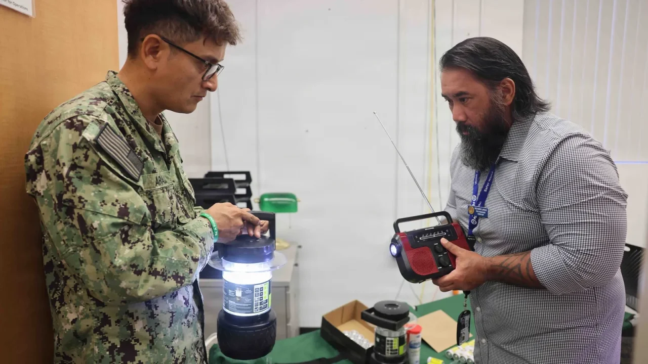 A Navy sailor and a civilian manager check a lantern and a hand-crank radio while preparing emergency kits for a hurricane exercise