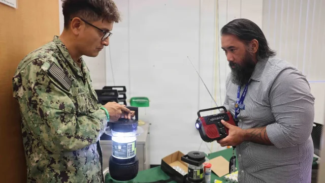 A Navy sailor and a civilian manager check a lantern and a hand-crank radio while preparing emergency kits for a hurricane exercise