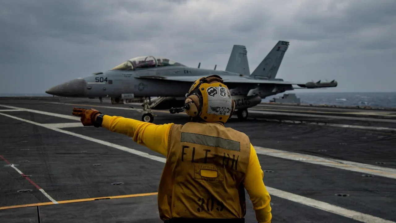 Sailor in a yellow jersey directs a jet on the flight deck of an aircraft carrier