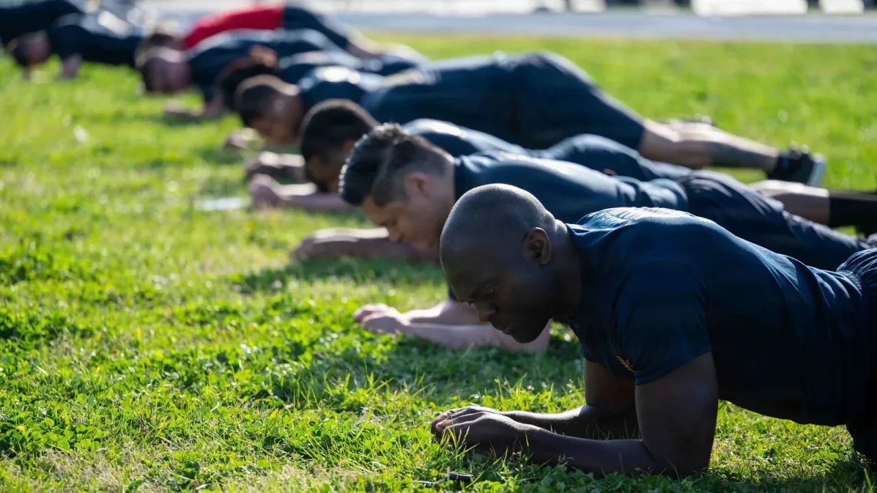 Row of sailors hold a forearm plank on grass during a physical readiness test