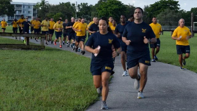 Group of sailors in Navy physical training uniforms run along a path during the cardio event of a fitness test