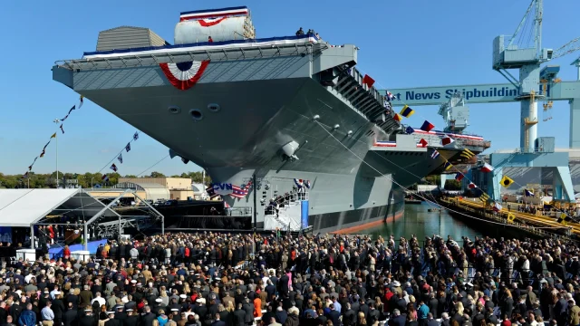 Crowd gathered beneath the bow of the aircraft carrier Gerald R. Ford, decorated with red, white and blue bunting, at its christening ceremony in November 2013